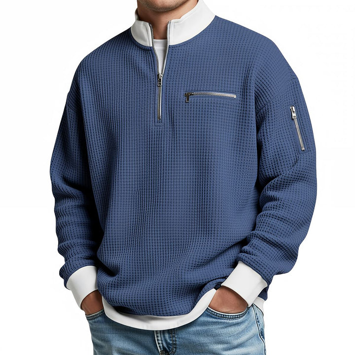 Pull gaufré bleu à col montant zippé, poche poitrine et poche zippée sur la manche, porté avec un jean. 3