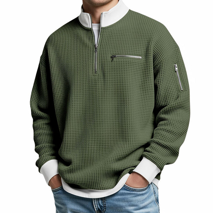 Pull gaufré vert kaki à col montant zippé, poche zippée poitrine et manche, porté de face avec un jean. 7
