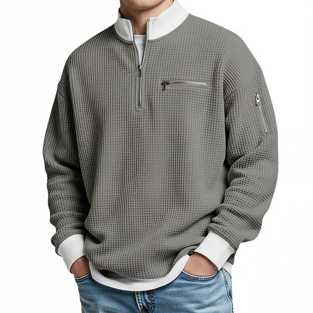Pull gaufré gris à col zippé, poignets et col blancs, porté de face avec un jean bleu clair. 8
