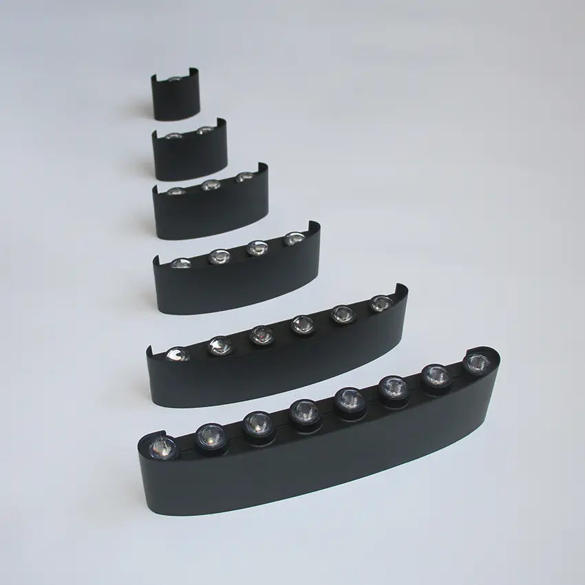 Les six appliques noires alignées en diagonale sur fond gris clair, de la plus courte à la plus longue, LED visibles sur le dessus. 10