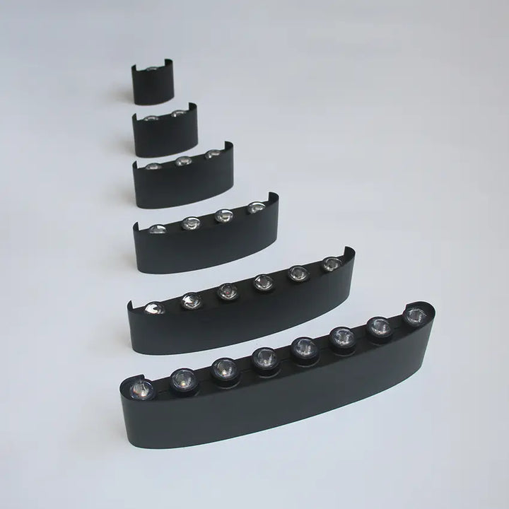 Les six appliques noires alignées en diagonale sur fond gris clair, de la plus courte à la plus longue, LED visibles sur le dessus. 10