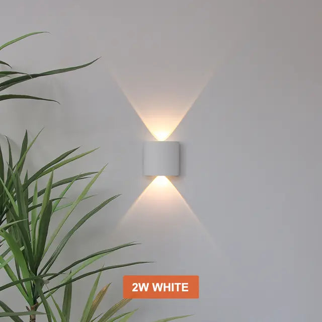Petite applique cylindrique blanche allumée sur un mur, projetant un faisceau de lumière chaude vers le haut et un vers le bas. 4