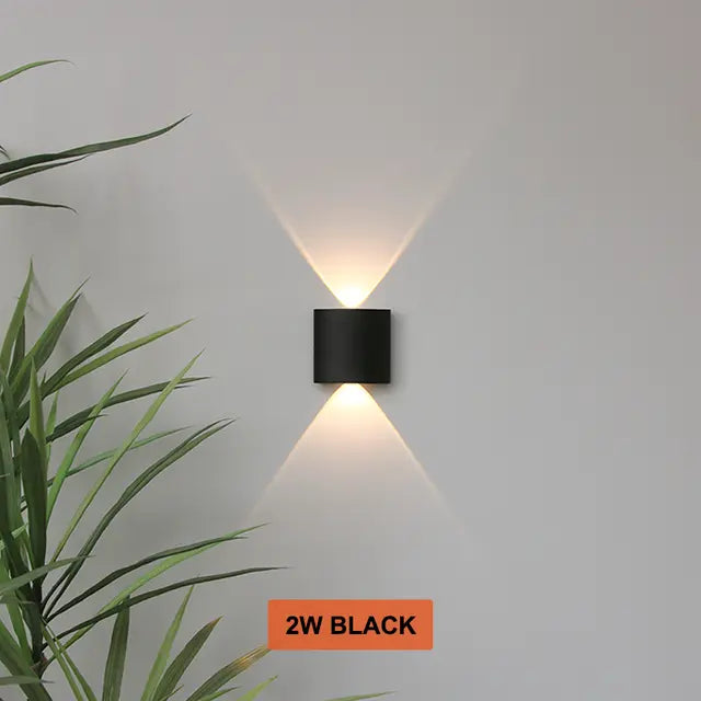 Petite applique cylindrique noire allumée sur un mur gris, avec un faisceau de lumière chaude vers le haut et un vers le bas. 5