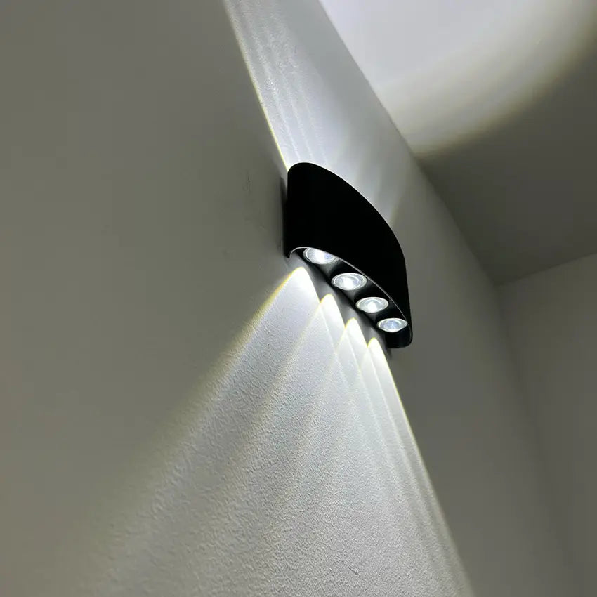 Applique noire vue d'en bas dans un angle de mur, quatre LED visibles et faisceaux de lumière blanche vers le bas. 2