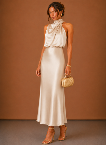 Femme de face portant la robe longue en satin champagne à col licou drapé, avec pochette tressée dorée. 4