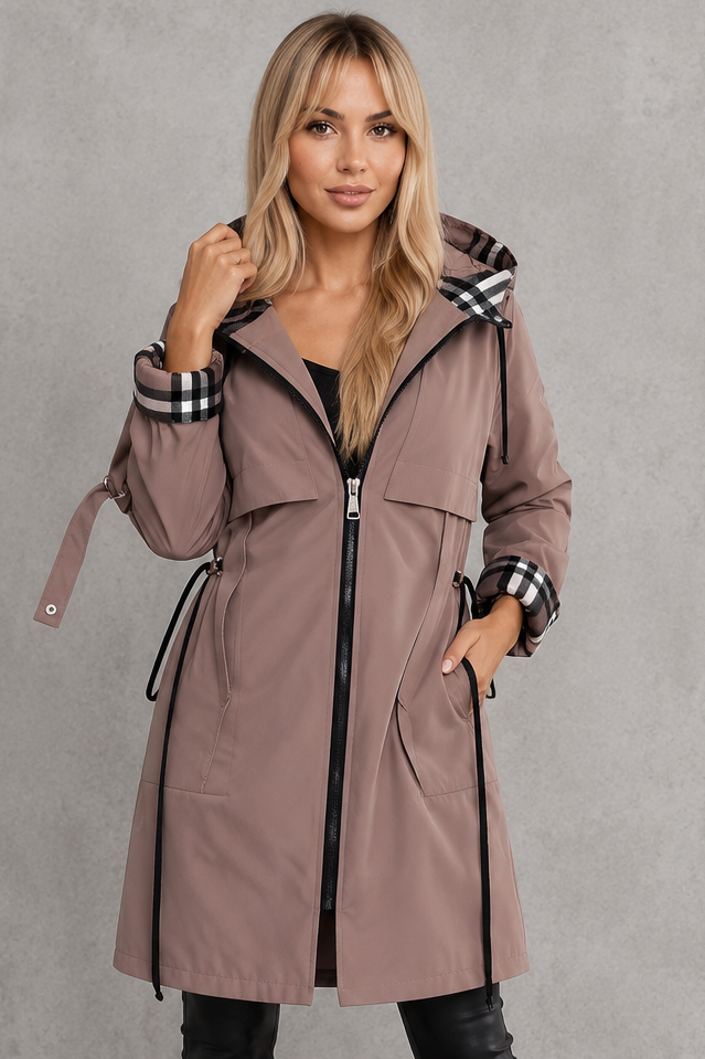Plan rapproché d'une femme portant l'imperméable taupe zippé, capuche relevée, avec doublure à carreaux visible aux poignets et dans la capuche. 1