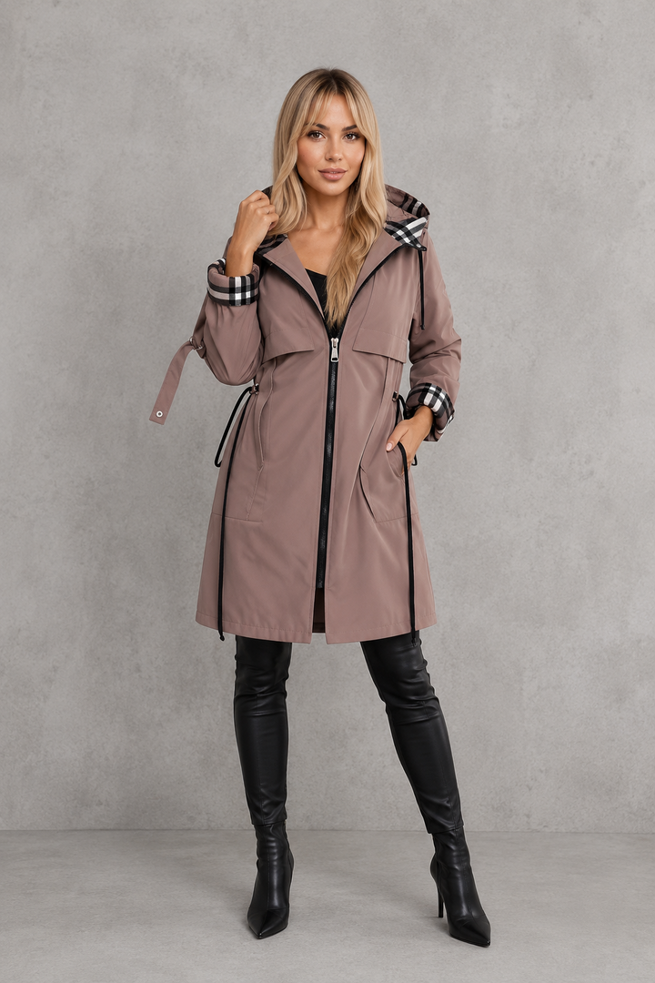 Femme en pied portant l'imperméable taupe zippé, cordons de taille noirs pendants, une main sur la capuche, avec bottes noires. 7