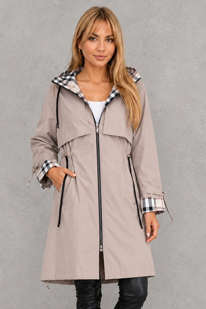 Femme portant l'imperméable beige clair zippé, taille ajustée par cordons noirs, capuche et poignets doublés à carreaux, vue de face. 2