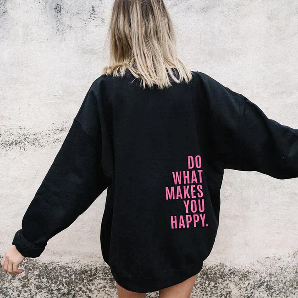 Vue de dos d'un sweat noir oversize porté par une femme blonde, bras écartés, avec un message imprimé en rose sur le côté du dos. 4