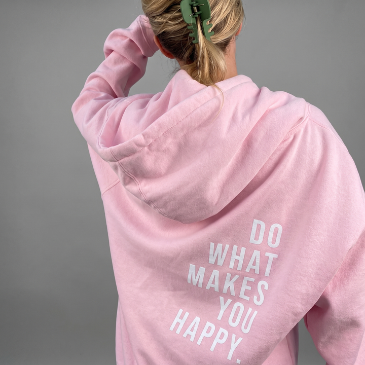 Vue de dos d'un sweat rose clair porté par une femme blonde, cheveux relevés par une pince verte, un bras plié vers la tête. 1