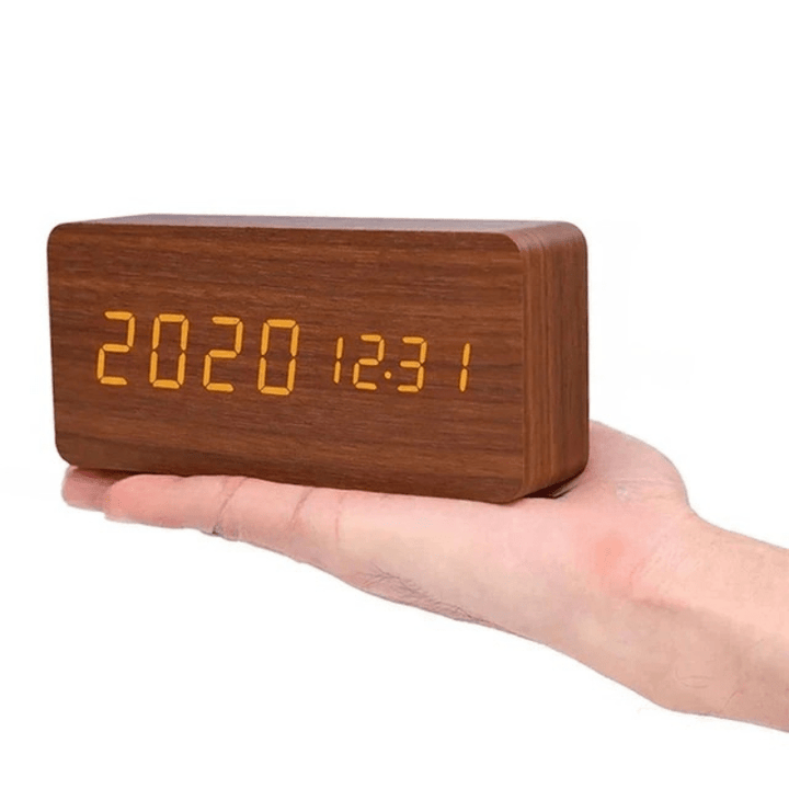 Réveil rectangulaire en bois brun tenu sur la main, affichage LED orange de la date plutôt que de l'heure. 13