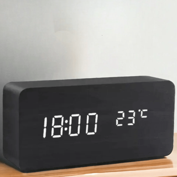 Réveil rectangulaire noir effet bois posé sur une surface en bois, affichage LED blanc de l'heure et de la température. 6