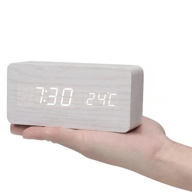 Réveil rectangulaire en bois blanc posé sur une paume de main, chiffres LED blancs de l'heure et de la température. 10