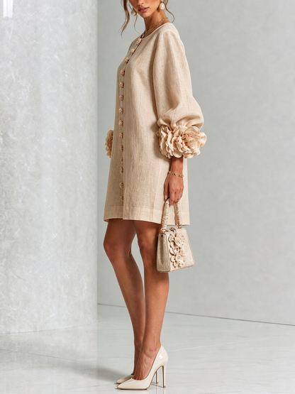 Robe beige portée de profil, manche ballon avec rosette au poignet, petit sac à main beige orné de fleurs. 28