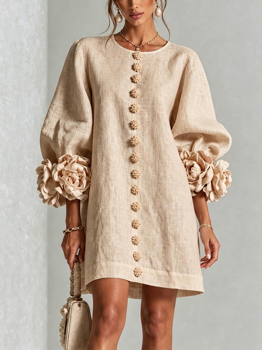 Gros plan de face sur la robe beige portée, boutons fleurs sur le devant et manches bouffantes terminées par de grosses fleurs. 23