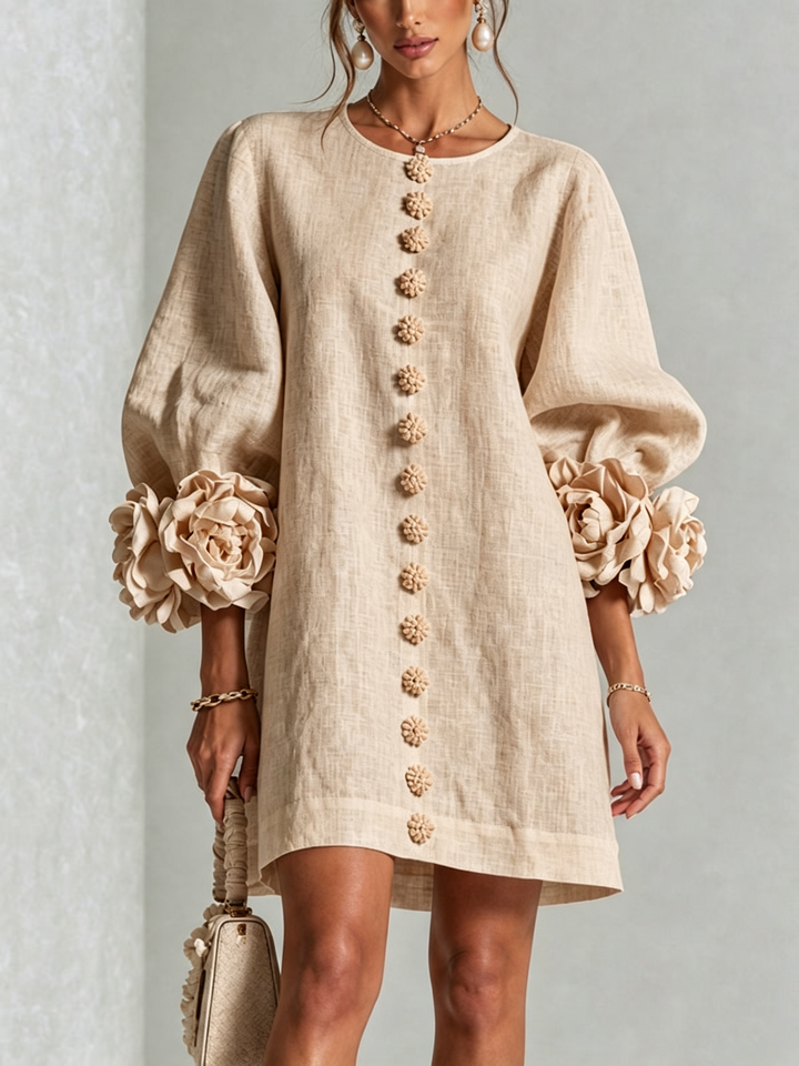 Robe beige en lin portée de face, rangée de boutons fleurs au centre et manches ballon bordées de grosses rosettes. 27