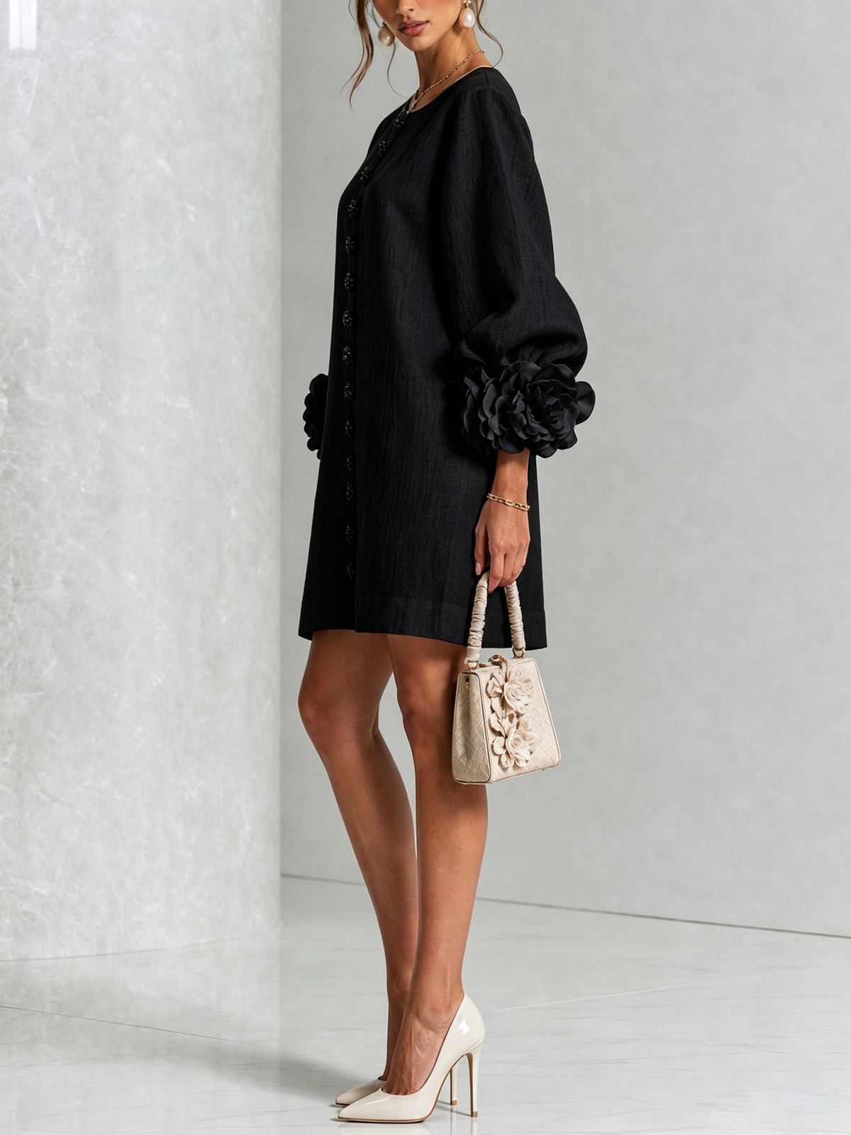 Robe noire portée de profil, manche ballon terminée par une grosse rose en tissu, avec sac à main beige et escarpins. 22