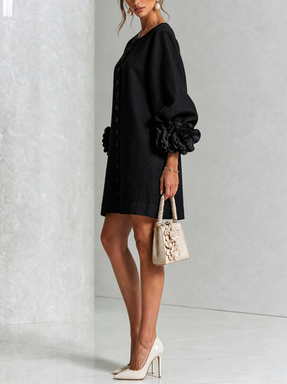 Robe noire portée de profil, manche ballon terminée par une grosse rose en tissu, avec sac à main beige et escarpins. 22