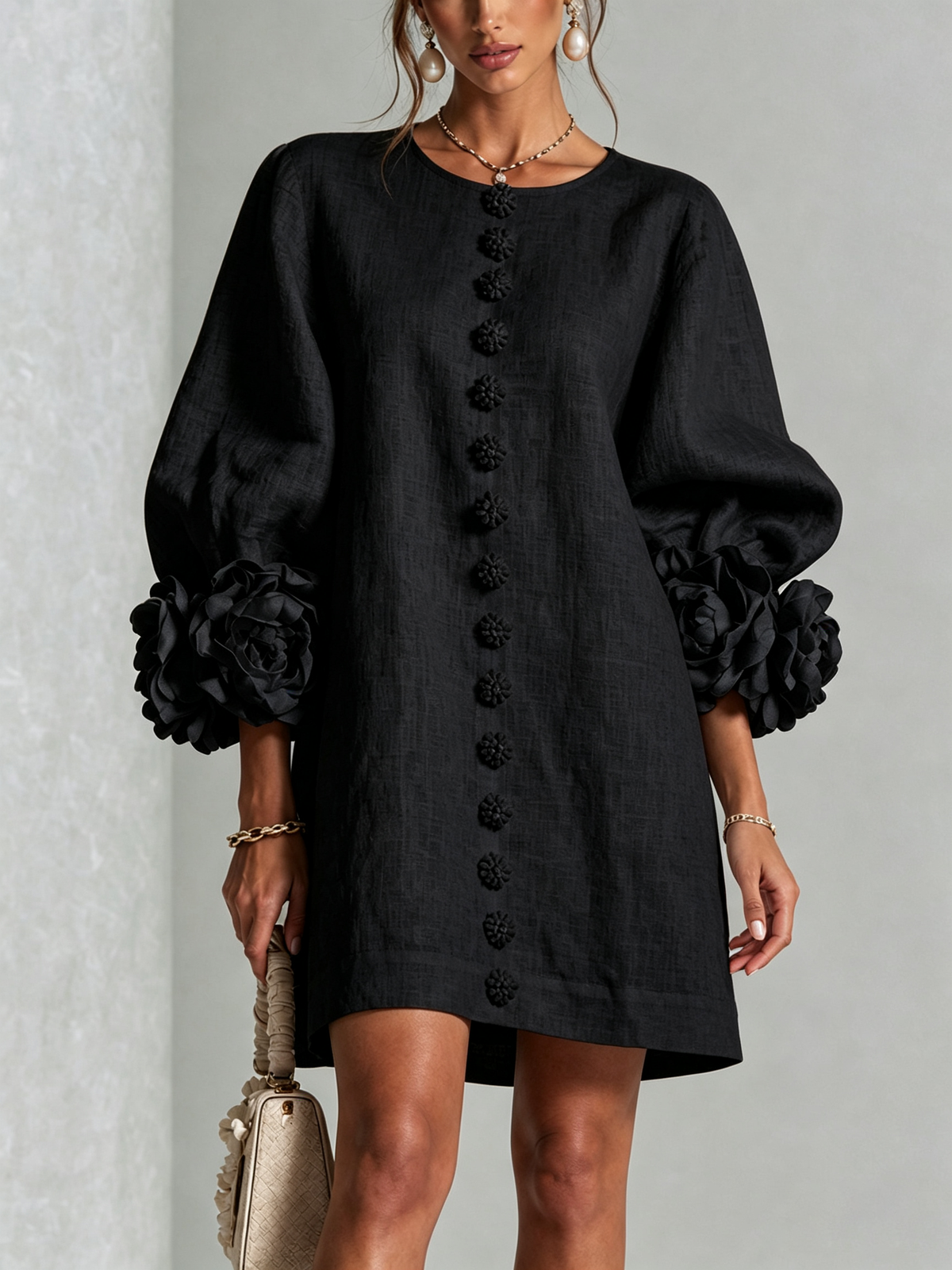 Robe noire portée en vue de face, avec rangée de boutons fleurs sur le devant et manches ballon ornées de grandes roses. 21