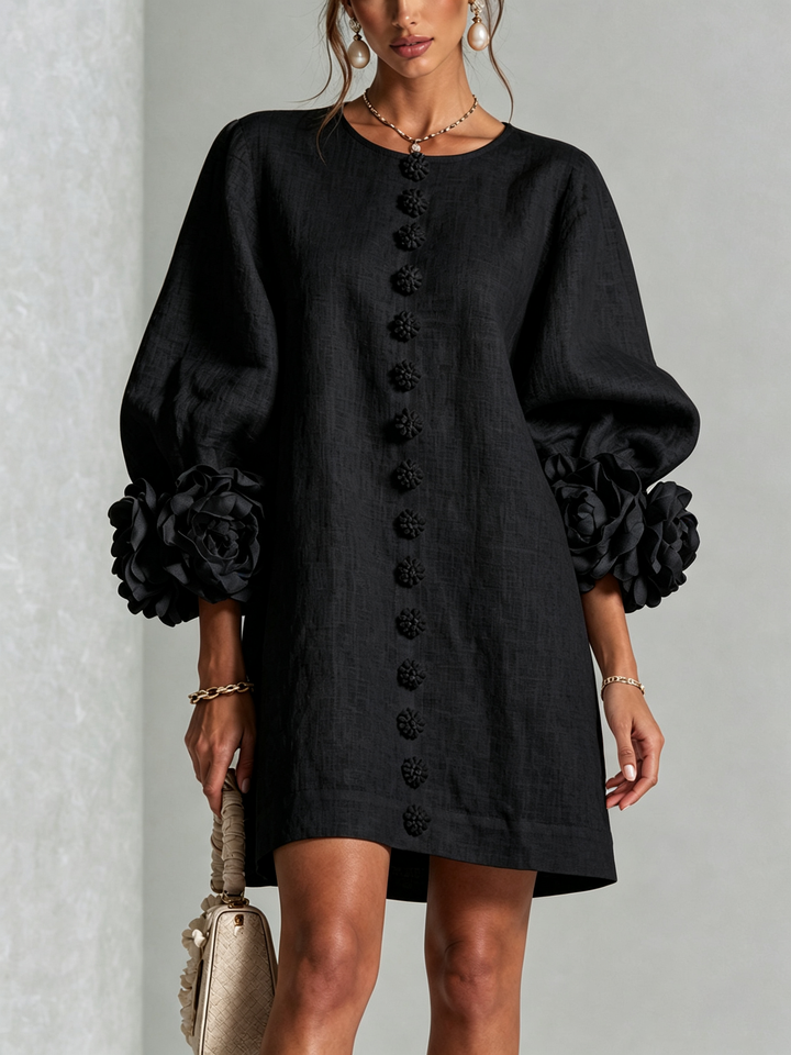 Robe noire portée en vue de face, avec rangée de boutons fleurs sur le devant et manches ballon ornées de grandes roses. 21