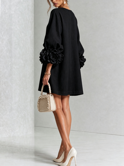 Robe noire portée de dos et de trois quarts, coupe droite ample, rosettes aux poignets, sac beige à volants. 23