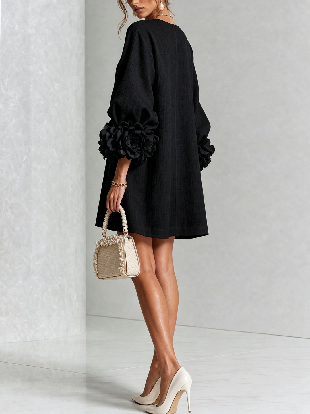 Robe noire vue de dos et de trois quarts, poignets fleuris volumineux, petit sac beige à volants tenu à la main. 17