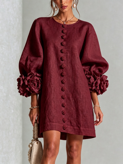 Robe bordeaux portée de face, boutons fleurs sur le devant et manches ballon terminées par de grandes rosettes. 38