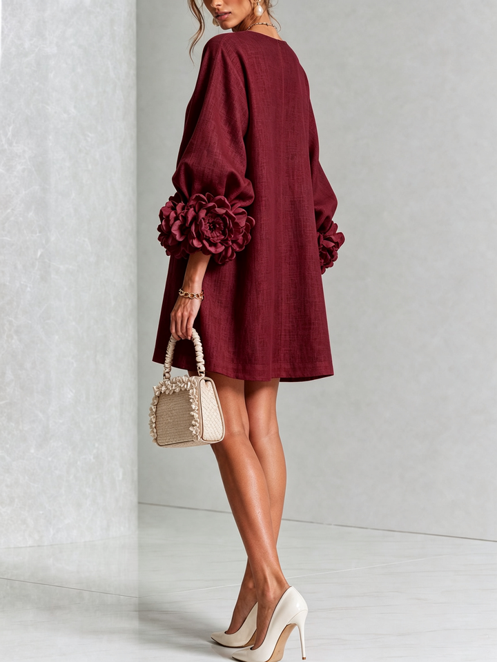 Robe bordeaux vue de dos et de trois quarts, coupe évasée, rosettes aux poignets, sac beige à volants. 40