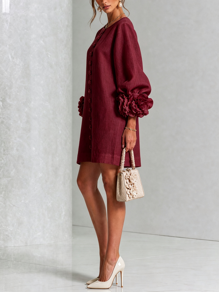 Robe bordeaux portée de profil, manche ballon avec grosse rosette au poignet, sac beige fleuri et escarpins clairs. 39