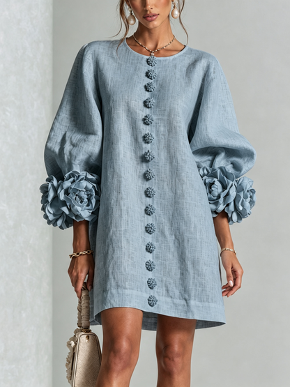 Vue de face de la robe courte bleu-gris portée par un mannequin, boutons en fleurs sur le devant et larges manches ornées de roses. 41