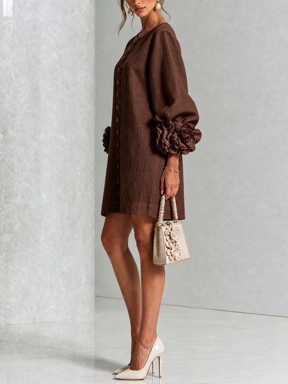 Robe marron portée de profil, manche ballon avec grosse rosette au poignet, sac beige fleuri et escarpins clairs. 32