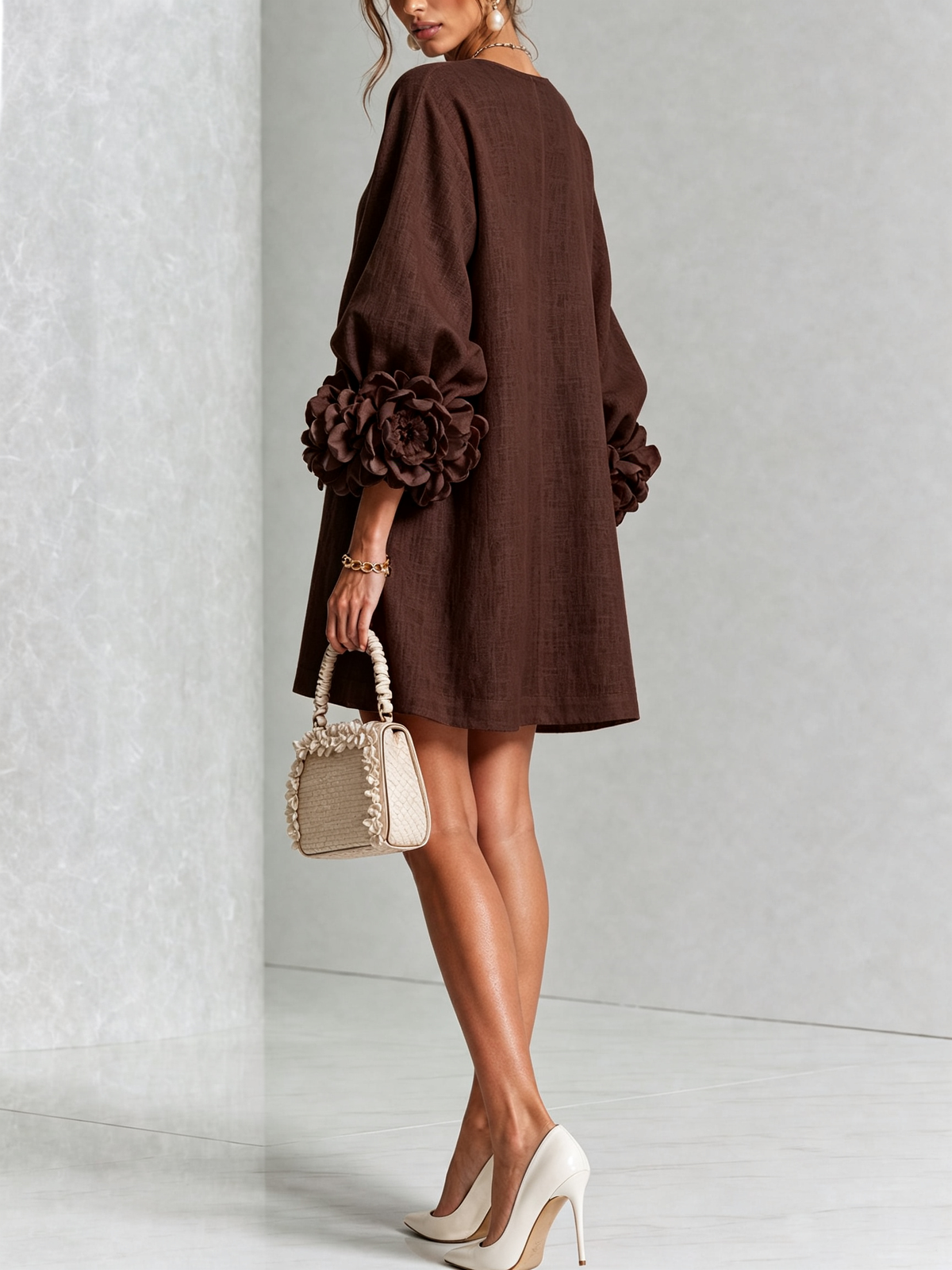 Robe marron vue de dos et de trois quarts, coupe évasée, rosettes aux poignets, petit sac beige à volants. 33