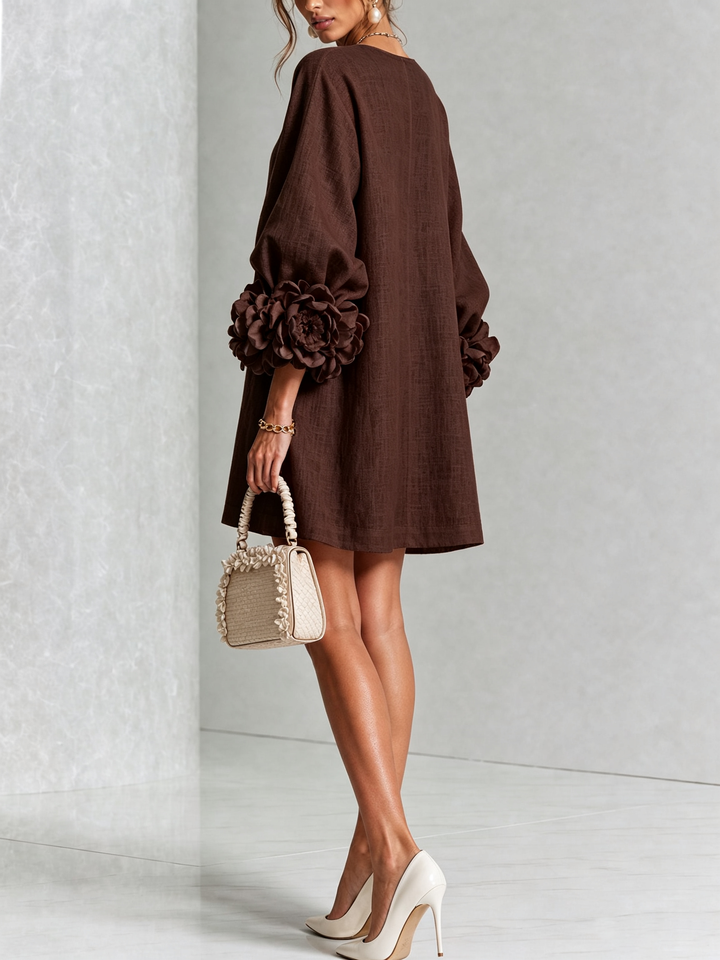 Robe marron vue de dos et de trois quarts, coupe évasée, rosettes aux poignets, petit sac beige à volants. 33