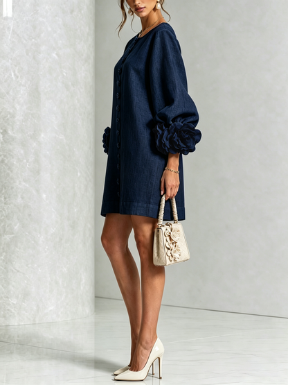 Robe bleu marine vue de profil en studio, avec escarpins clairs, petit sac beige et rose à la manche. 19