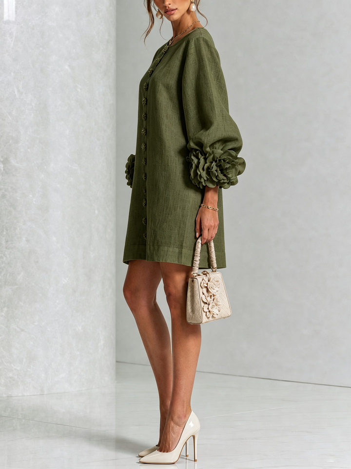 Robe verte portée de profil, manche bouffante terminée par une grosse fleur, avec sac à main beige et escarpins clairs. 8