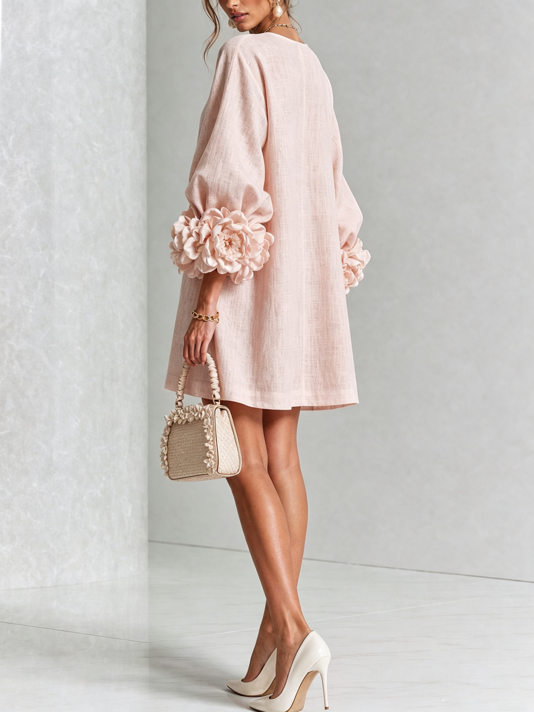 Robe rose poudré vue de dos, coupe évasée, rosettes aux poignets, mannequin tenant un petit sac beige à volants. 26