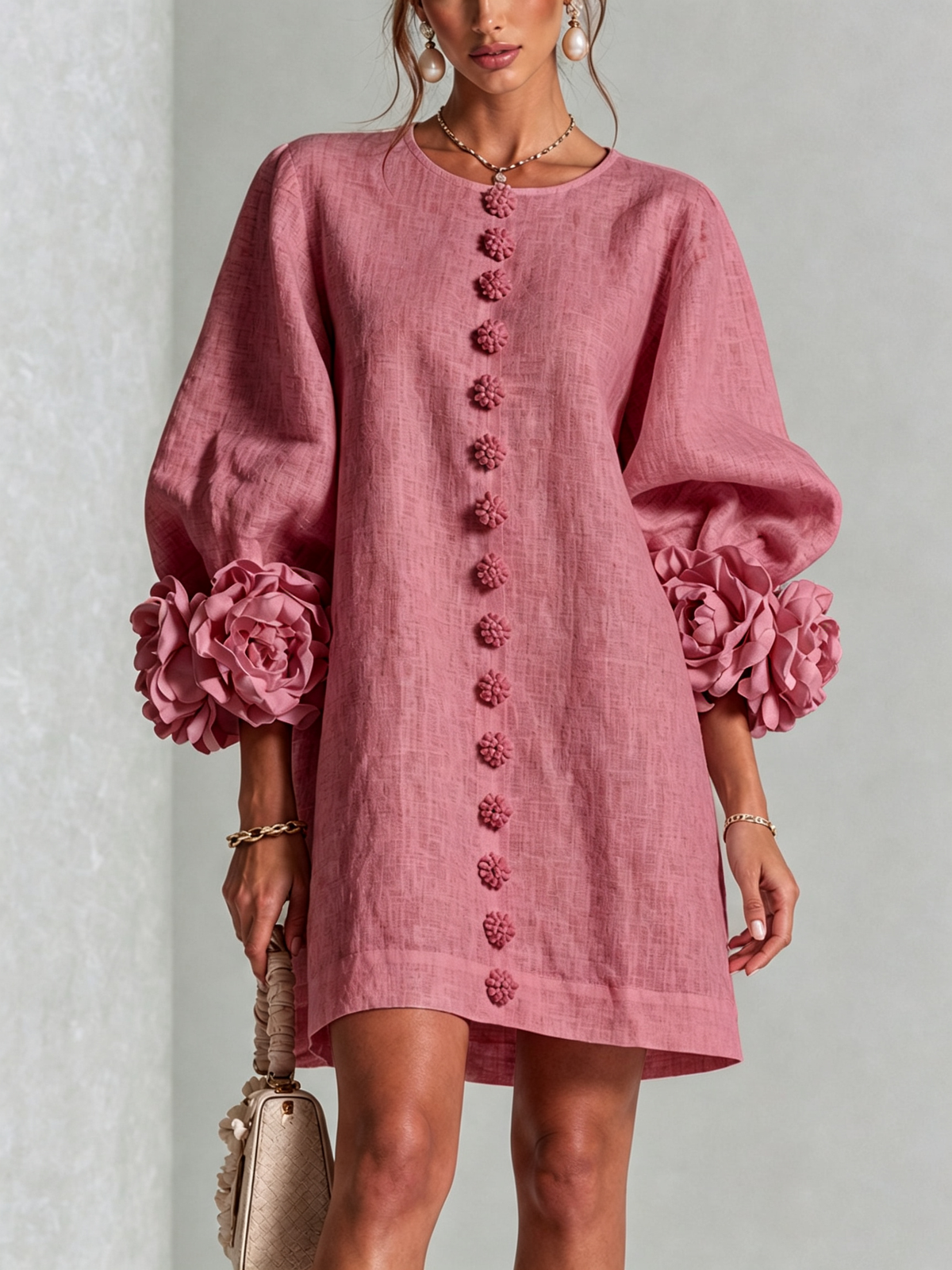 Vue de face de la robe rose portée par un mannequin, rangée de boutons en forme de fleurs et manches ballon à rosettes. 44