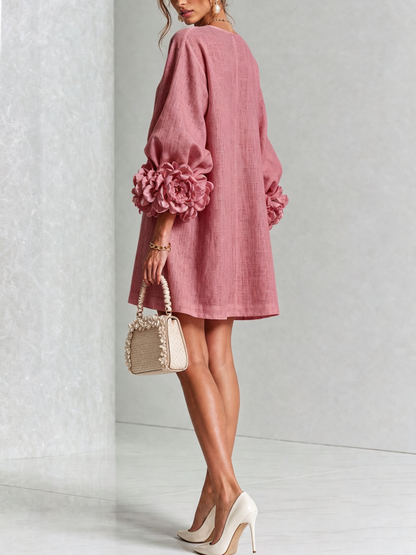 Vue de dos de la robe rose, mannequin tournée de côté, coupe droite et rosettes en tissu aux poignets des manches. 46