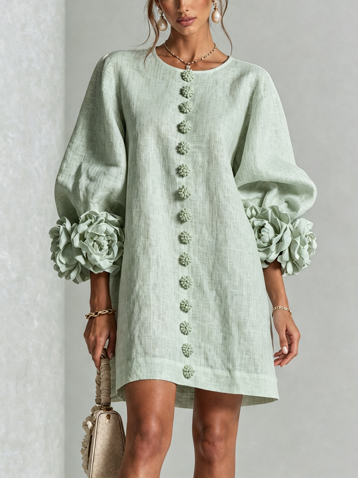 Robe vert d'eau portée de face, rangée de boutons fleurs au centre et manches ballon ornées de grandes rosettes. 35
