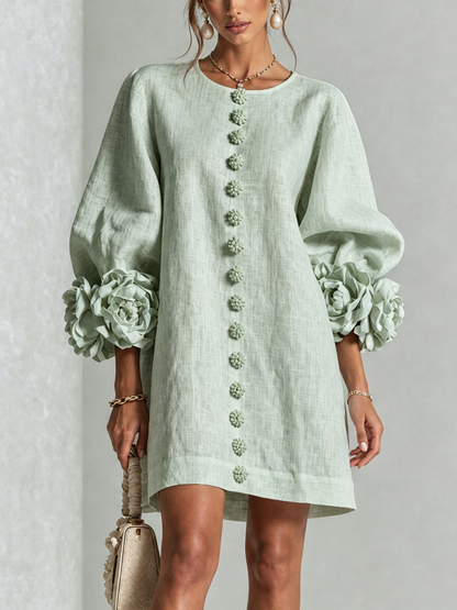 Robe vert d'eau portée de face, rangée de boutons fleurs au centre et manches ballon ornées de grandes rosettes. 35