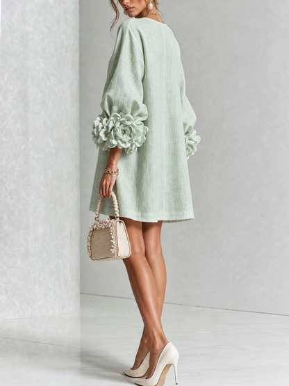 Robe vert d'eau vue de dos, coupe ample, rosettes aux poignets, mannequin avec petit sac beige à volants. 37