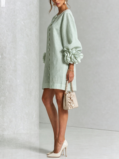 Robe vert d'eau portée de profil, manche ballon avec grosse rosette au poignet, sac beige fleuri et escarpins vernis clairs. 36