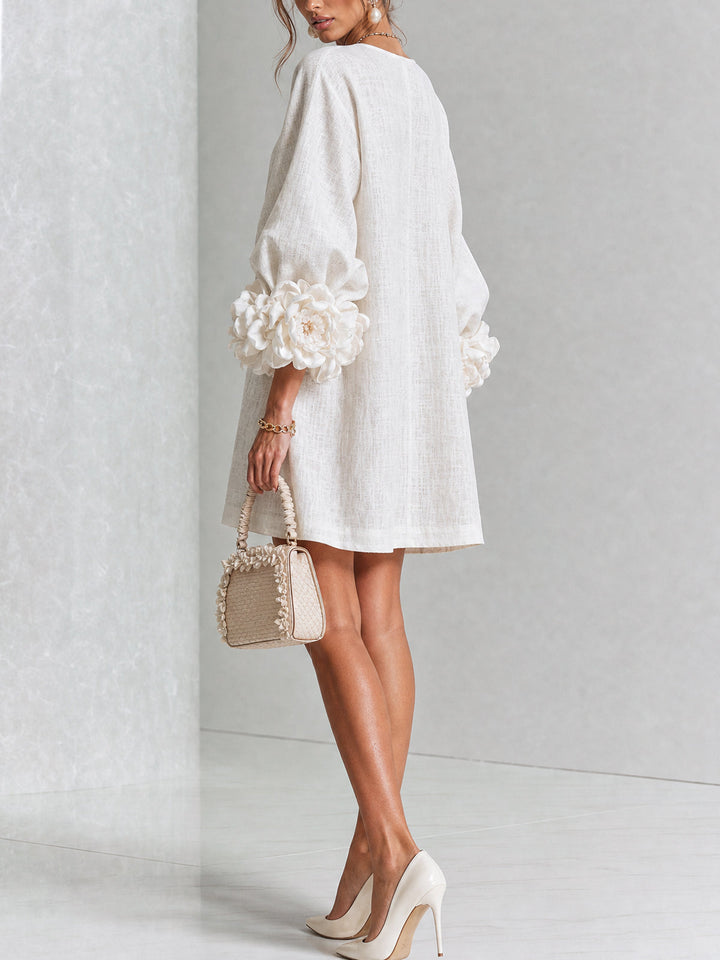 Robe crème vue de dos et de trois quarts, avec poignets fleuris volumineux et petit sac beige tenu à la main. 3