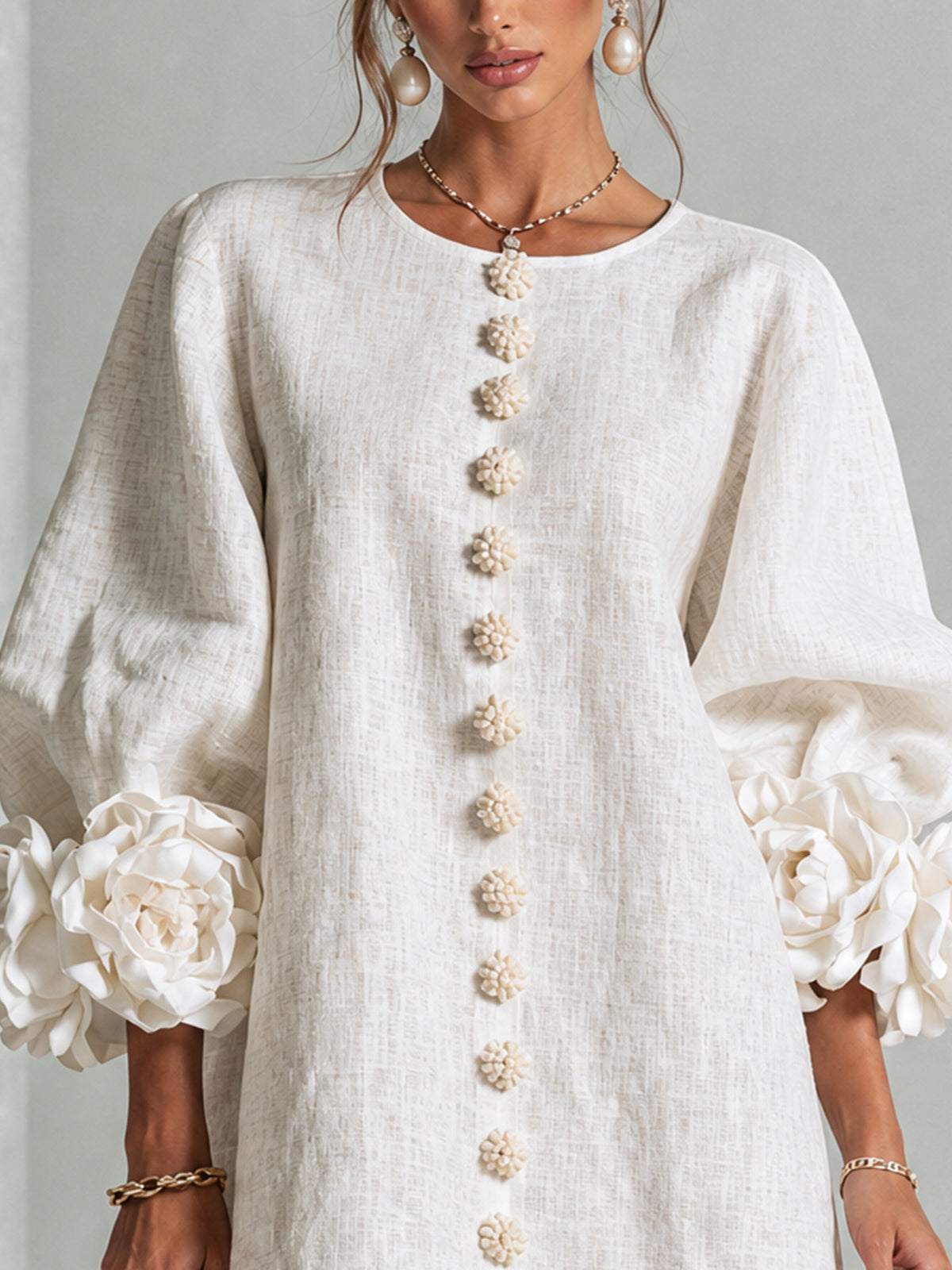 Gros plan sur le buste de la robe écrue: encolure ronde, boutons fleurs en rangée et roses aux manches. 15