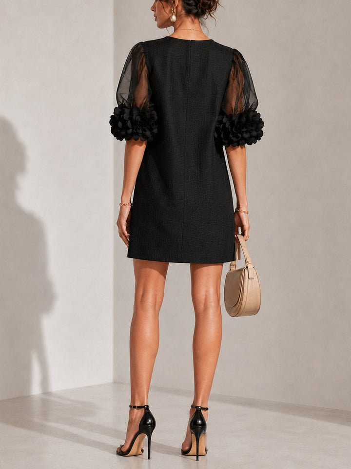 Robe noire vue de dos avec fermeture centrale, manches transparentes ornées de fleurs, portée avec des sandales à talons noires. 3