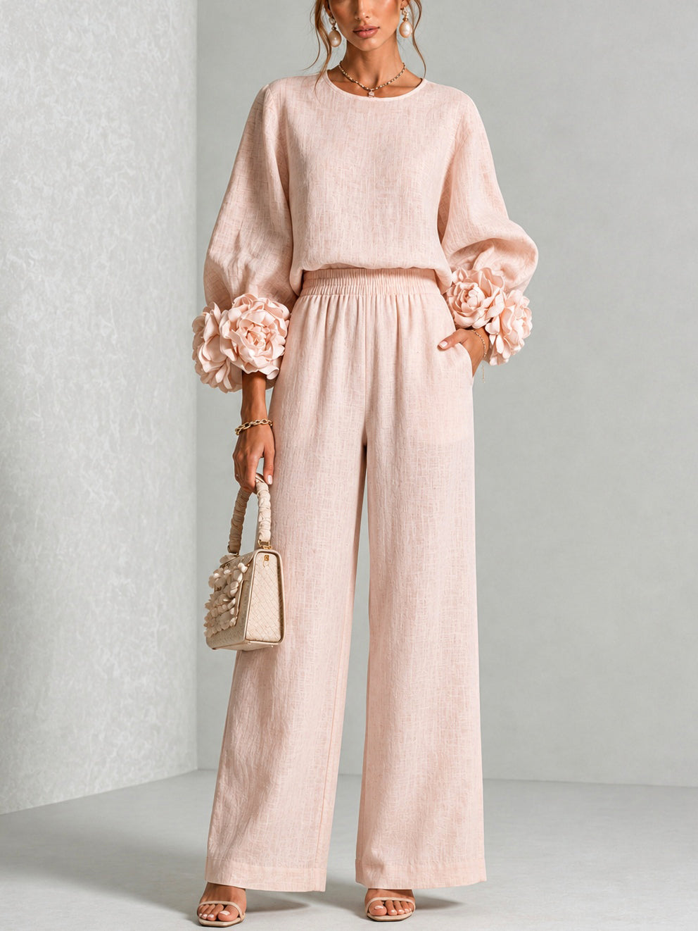 Ensemble rose pâle porté en pied avec grandes fleurs aux poignets, pantalon large et sac tressé 1