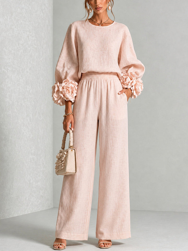 Ensemble rose pâle porté en pied avec grandes fleurs aux poignets, pantalon large et sac tressé 1