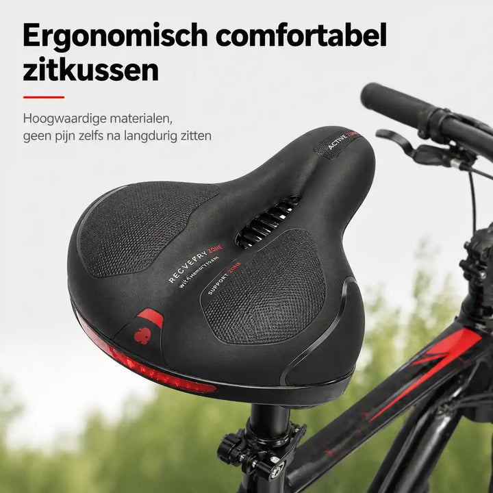 Selle noire à découpe centrale et bande réfléchissante rouge, montée sur un vélo tout-terrain devant un fond de verdure. 1
