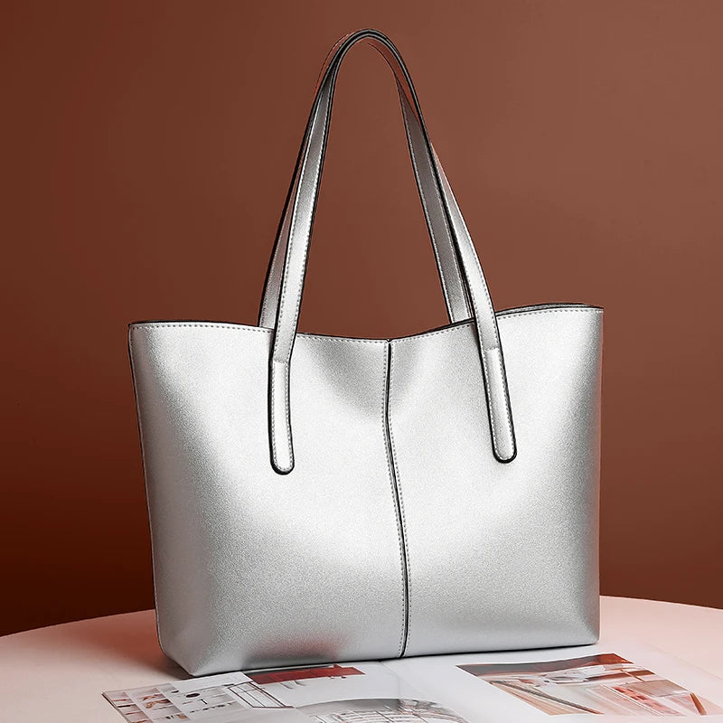 Sac cabas argenté posé en biais sur une table, devant un mur brun, magazine ouvert dessous 2