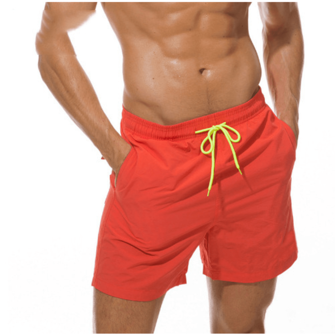 Short de bain rouge orangé porté, cordon jaune fluo, les deux mains dans les poches latérales. 6